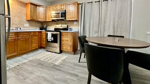 A compact kitchen with wooden cabinets, a microwave, an oven, and a dining area with a round table and chairs.