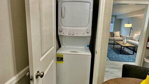 A compact, white washer and dryer unit in a small room with a door leading to a living area.