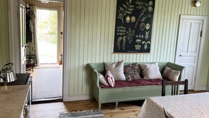 A room with a green sofa, a table with a tablecloth, a framed botanical illustration on the wall, and a door leading outside. - Summer house with secluded location in Julita   SE14028 (Julita)