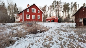 A red wooden house with a porch and a garage, surrounded by a snowy landscape and tall trees. - Summer house with secluded location in Julita   SE14028 (Julita)
