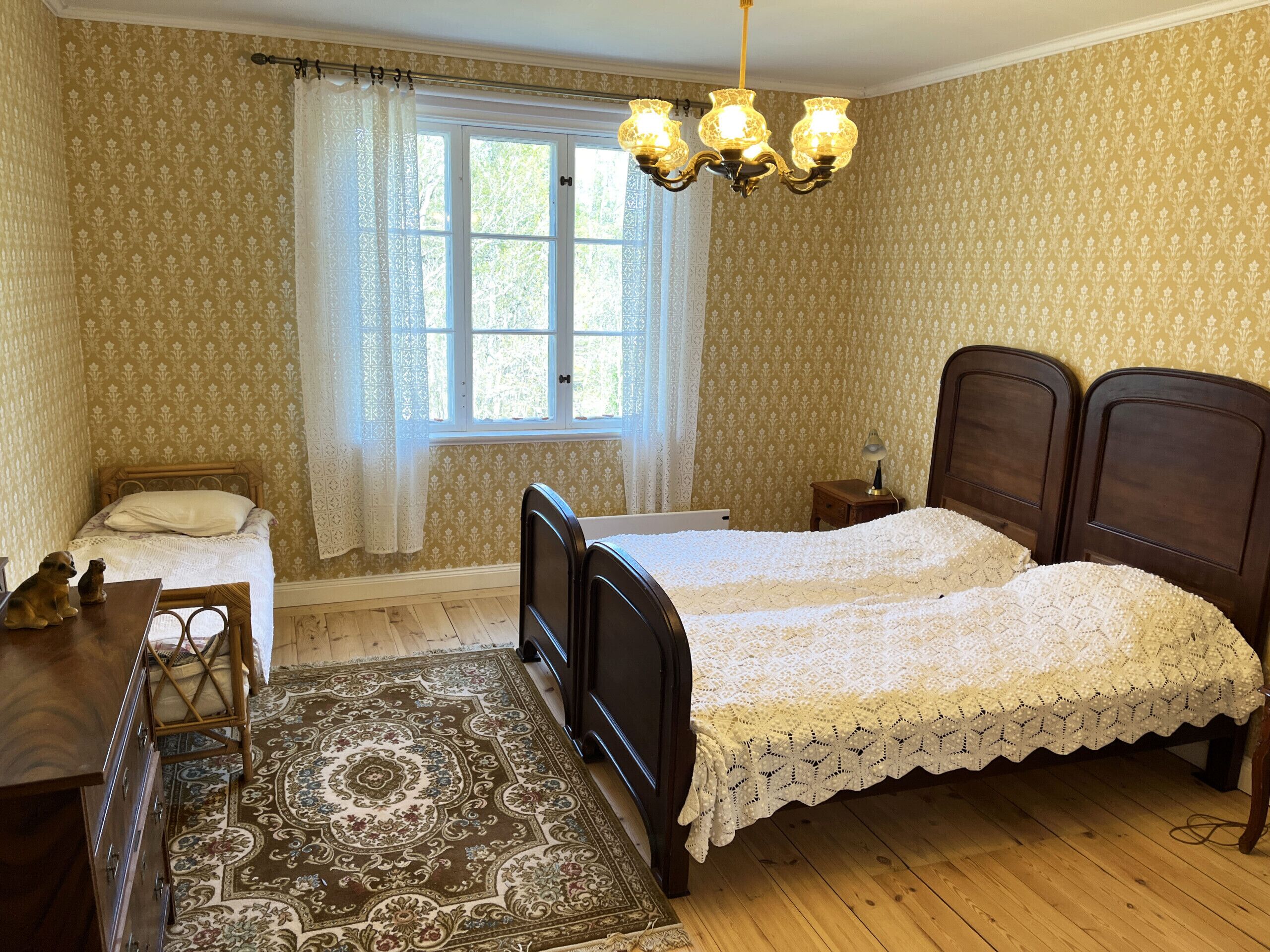 Un dormitorio con dos camas, un aparador de madera, una mesita de noche, una lámpara y una ventana con cortinas.