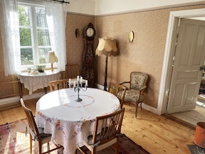 Une salle à manger avec une table ronde, des chaises, une horloge et une fenêtre avec des rideaux.