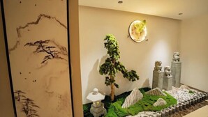 Un jardín japonés tradicional con un farol de piedra, un árbol bonsái y una escultura de león.