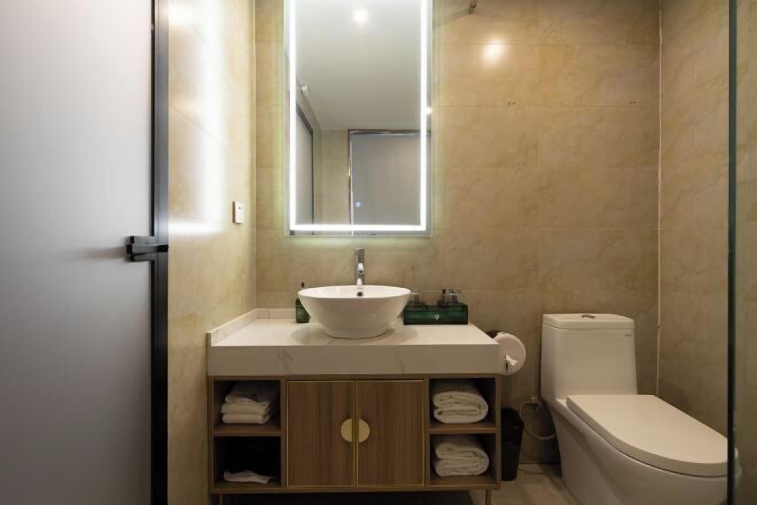 A modern bathroom with a large mirror, a white sink, a toilet, and a glass shower enclosure.