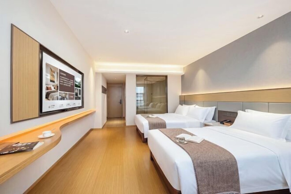 Habitació d'hotel amb dos llits, un escriptori, una televisió i una porta que fa a un passadís.