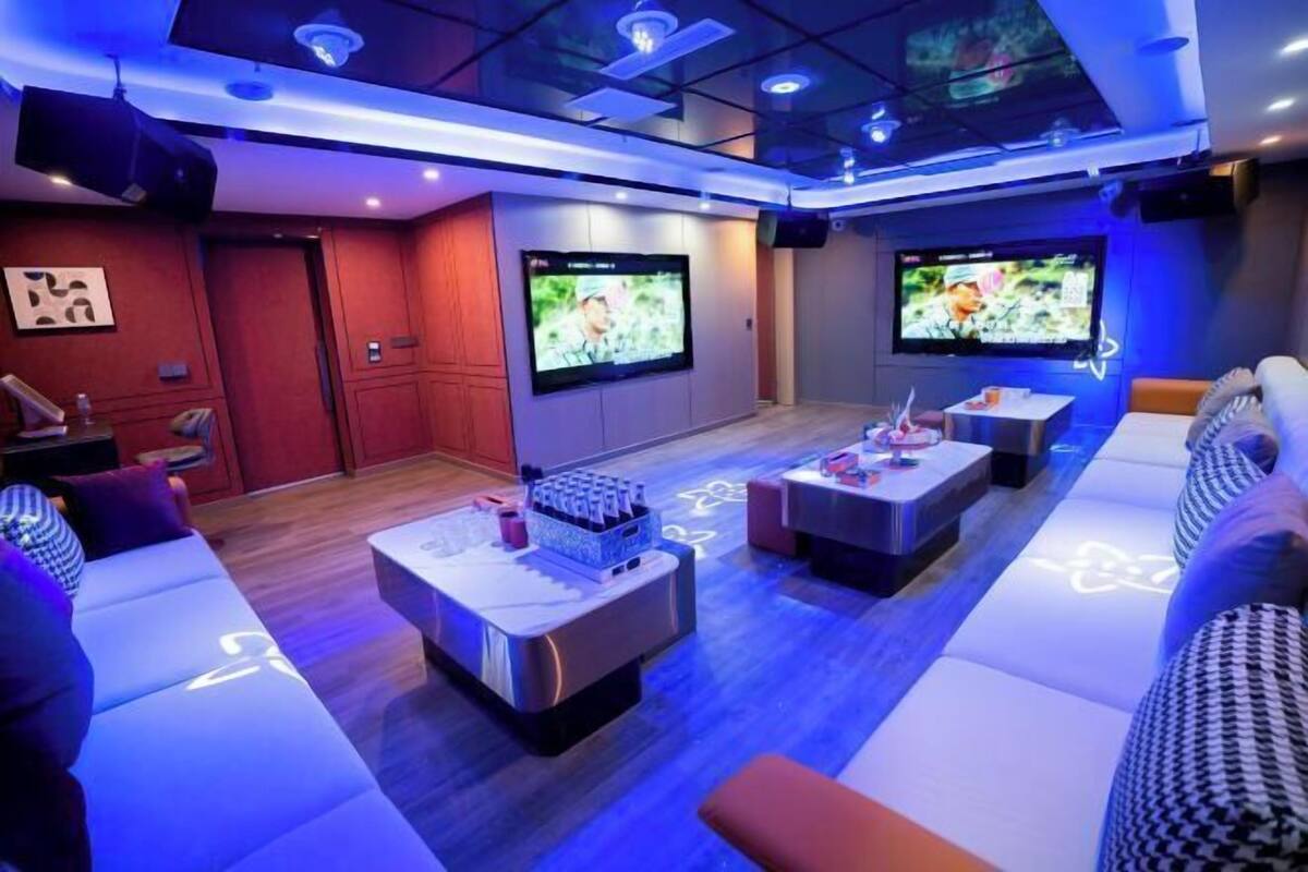 Un salón moderno con varias zonas de estar, televisores de pantalla plana en las paredes e iluminación ambiental.