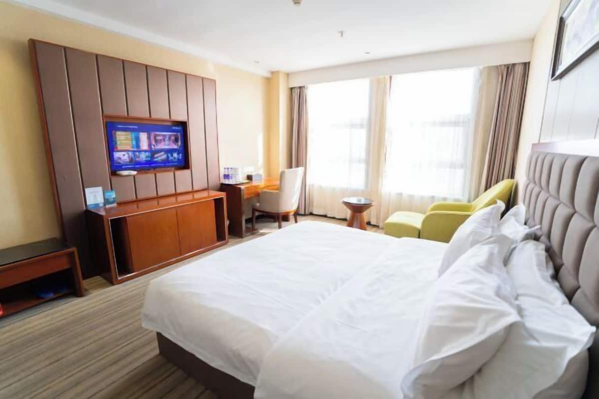 Una habitación de hotel con una cama grande, un televisor en la pared, un escritorio y una silla.