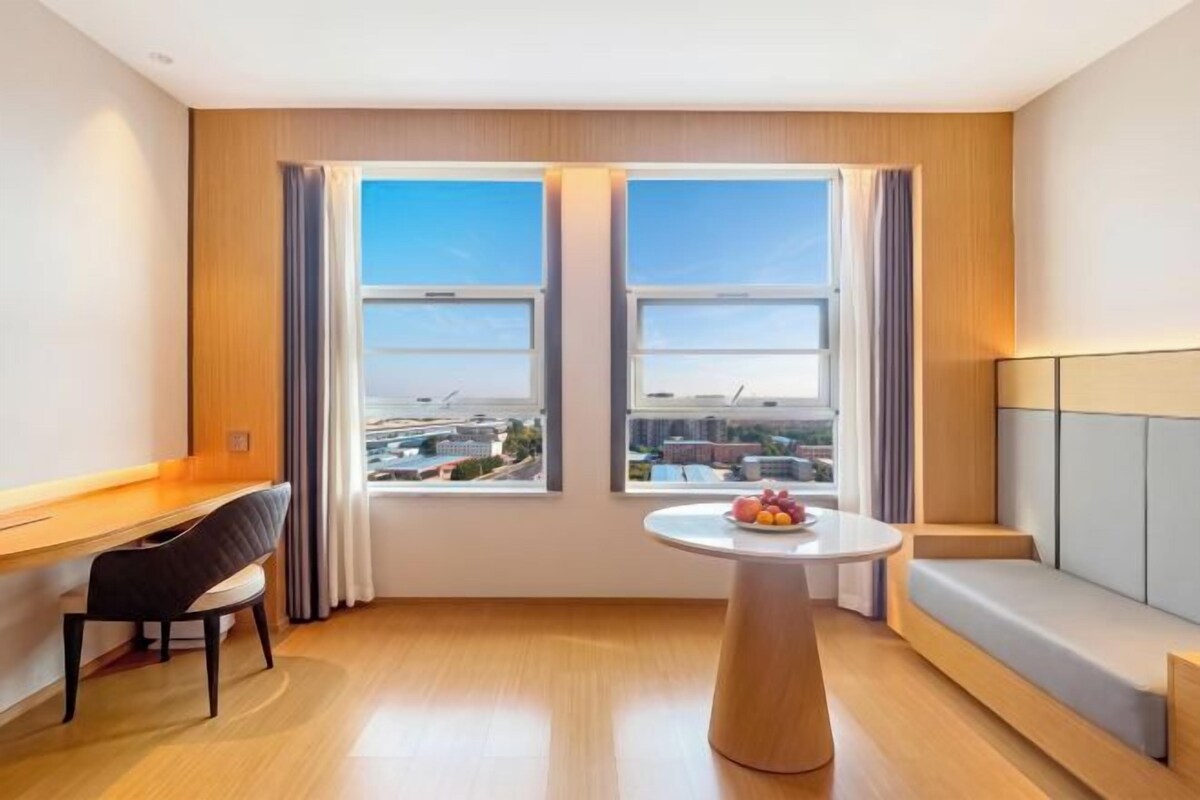 Een moderne hotelkamer met een groot raam, een ronde eettafel, een bank en een bureau.