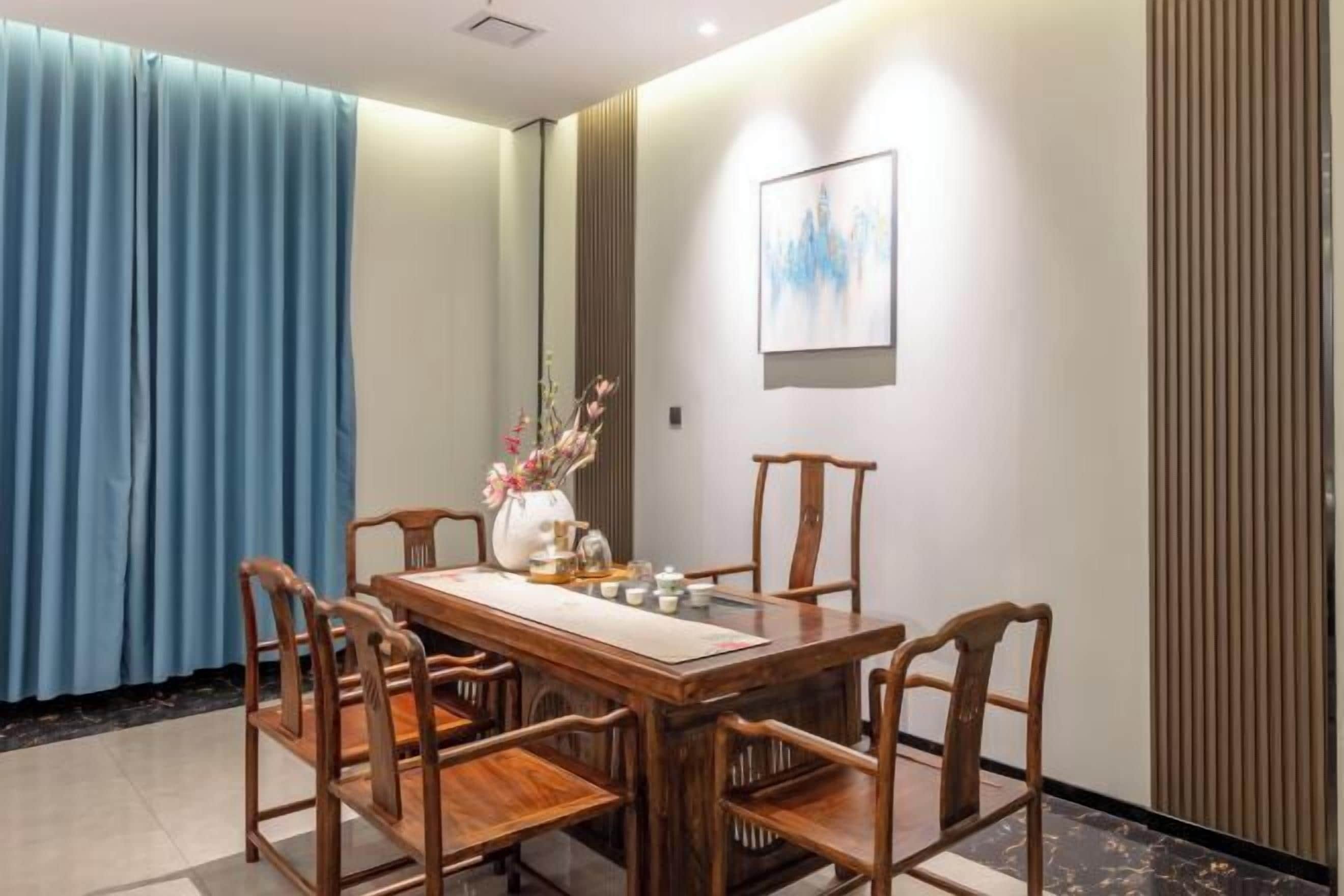 A dining area with a wooden table and chairs, a vase with flowers, and a framed picture on the wall.