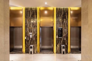Een lift met marmeren wanden en gouden accenten, voorzien van een bedieningspaneel en noodknoppen.