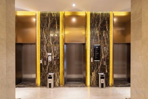 En elevator med marmorvægge og guldudsmykning, udstyret med kontrolpanel og nødknapper.