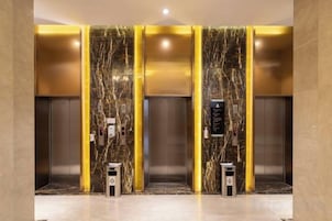 An elevator with marble walls and gold accents, equipped with a control panel and emergency buttons.