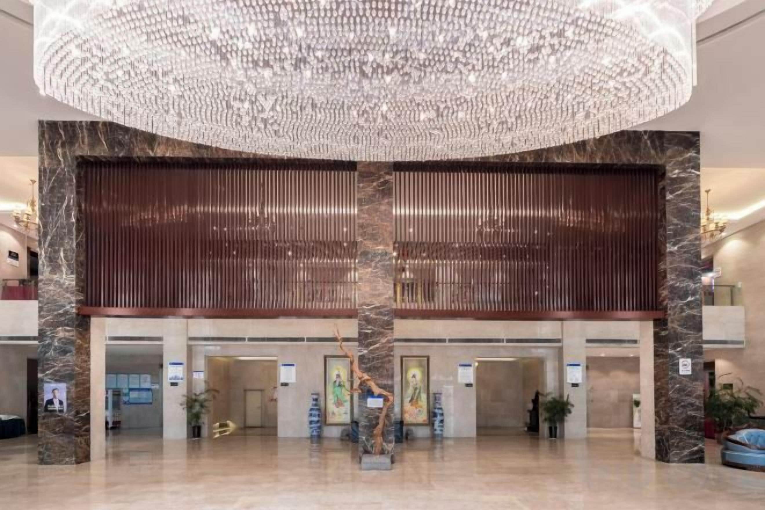 Un vestíbul espaiós amb un gran candelabro, columnes de marbre i un taulell de recepció modern.