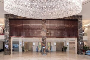 A spacious lobby with a large chandelier, marble columns, and a modern reception desk.