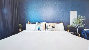 A bedroom with a geometric patterned wall, a bed with white bedding, two bedside tables with plants, and a blue chair. - Elgin Oasis Suite B (Elgin)