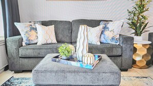 A grey sofa with patterned cushions, a small potted plant, and decorative items on a tray. - Elgin Oasis Suite B (Elgin)