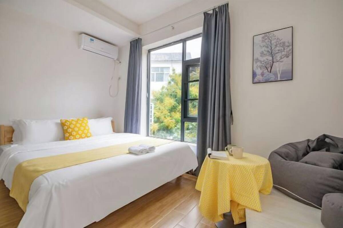 A hotel room with a bed, a small table with a cup, and a gray sofa.