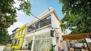Un edificio de dos pisos con balcón, ventanas amplias y un espacio al aire libre cubierto con una mesa y sillas.