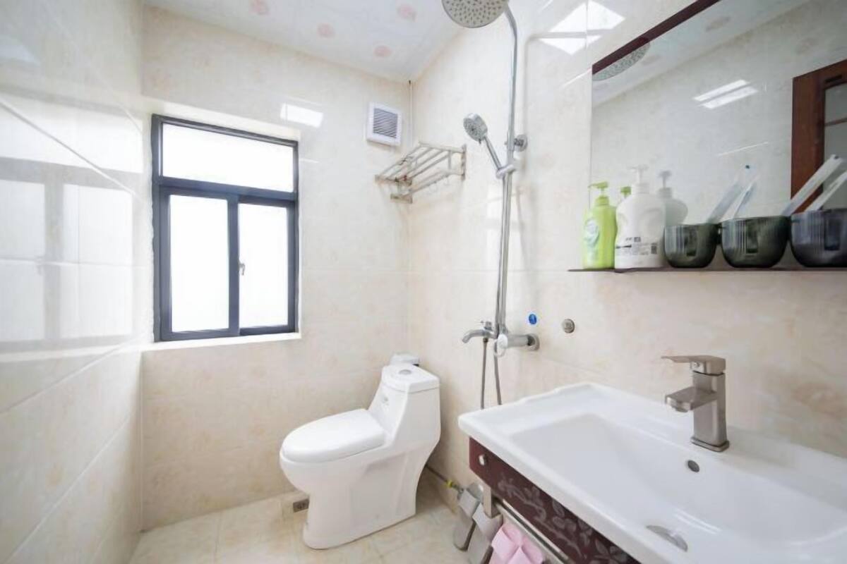 A bathroom with a toilet, a sink, and a shower. There is a window and a mirror on the wall.