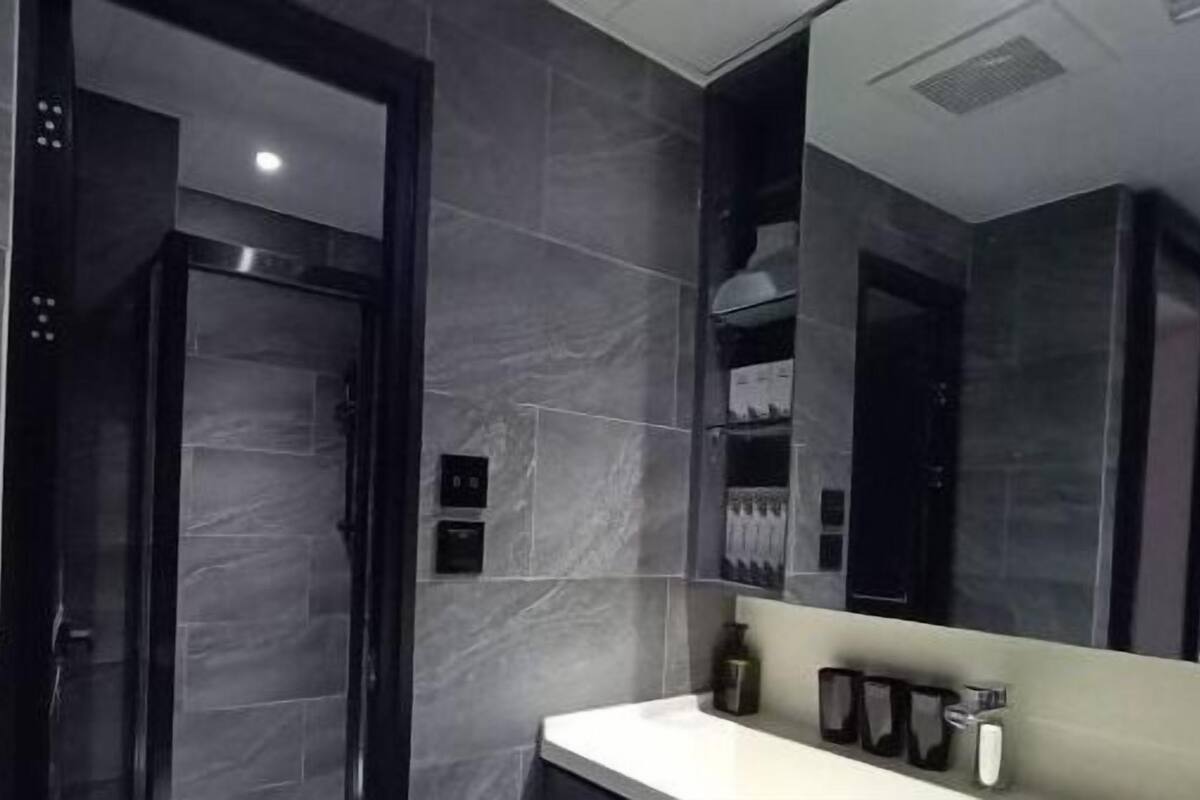 A modern bathroom with dark marble walls, a white sink, and a large mirror.