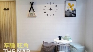 Ein Zimmer mit weißer Ziegelwand, einer Uhr, einem gerahmten Bild und einem kleinen, runden Tisch mit einem Stuhl.