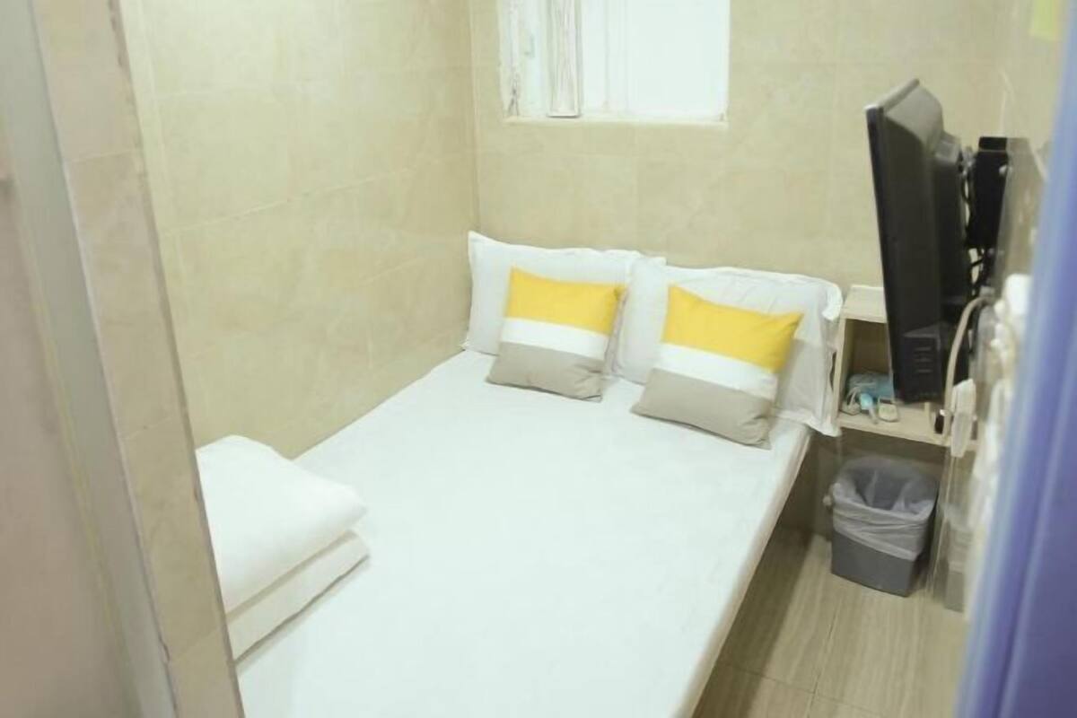 A small, neatly arranged room with a bed, a television, and a trash bin.