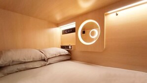 Ein kompakter, moderner Raum mit einem Bett, einer runden Leuchte und einer Bedienkonsole an der Wand.