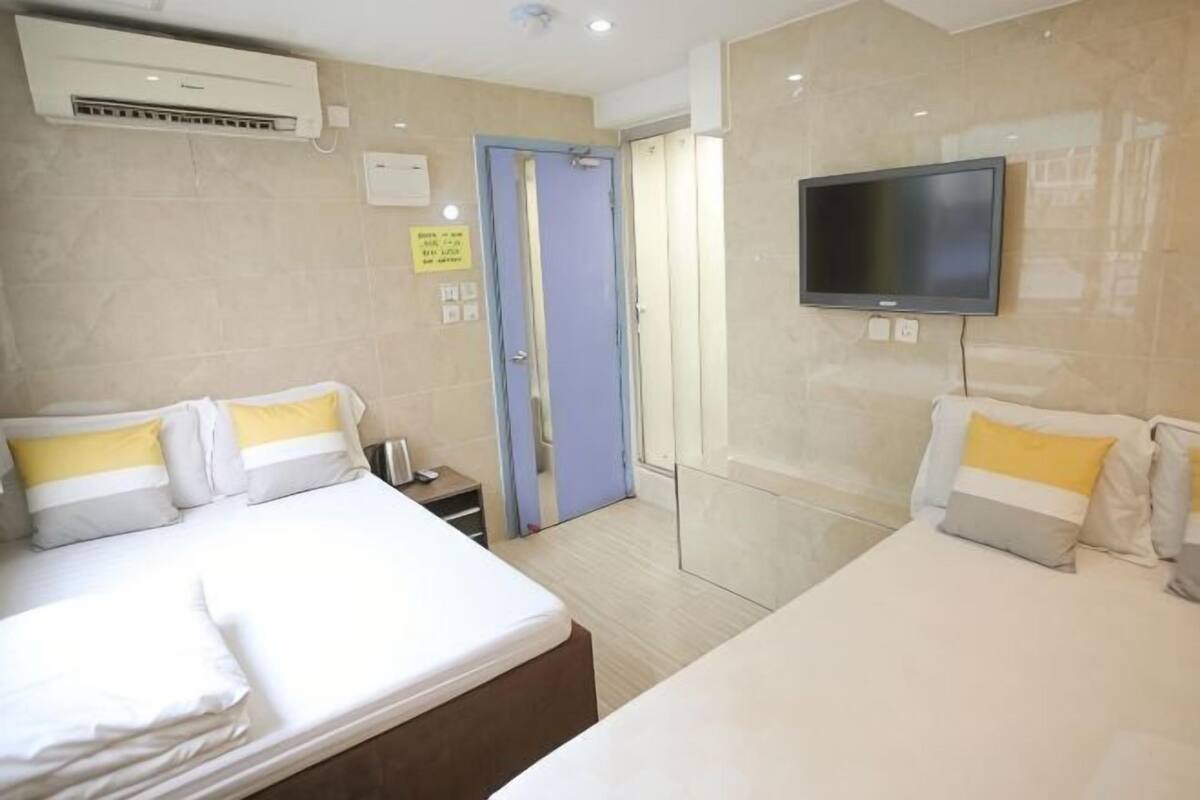 A hotel room with two beds, a television, an air conditioning unit, and a door leading to a bathroom.