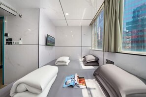 Ett hotellrum med två sängar, ett fönster med gardiner, en tidning på golvet och en tavla på väggen.