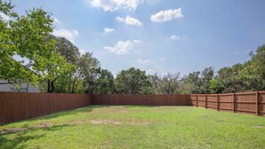 A backyard with a wooden fence, grass, and trees. - Luxury upgraded, high ceiling home near Domain, high tech corrida, businesses. (Austin)