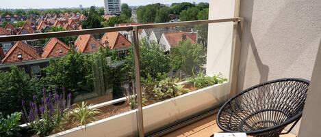 A balcony with a view of a residential area, a black chair, and a table with a white mug.