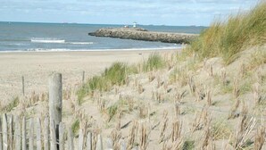 A sandy beach with a rocky outcrop and a wooden fence in the foreground. - 3-bedroom Holiday Home in Den Haag (The Hague)