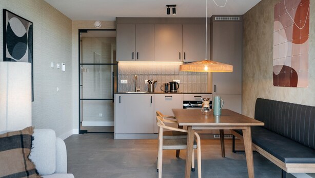 A modern kitchen with grey cabinets, a wooden dining table, and a bench. - 3-bedroom Holiday Home in Den Haag (The Hague)