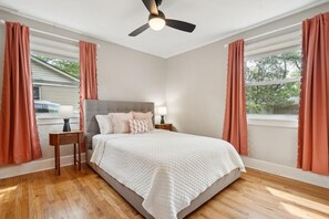 A bedroom with a bed, nightstands, a ceiling fan, and windows with curtains.