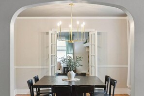 A dining area with a wooden table, black chairs, a white vase with greenery, and a chandelier.