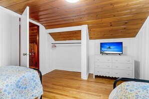 A room with wooden ceiling beams, a television on a dresser, and two beds with floral bedspreads.
