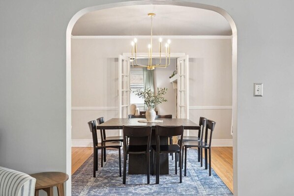 A dining area with a rectangular table, six chairs, a chandelier, and a blue patterned rug.