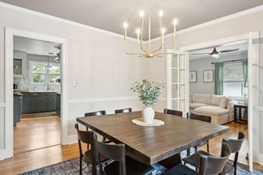 A dining area with a wooden table, chairs, a chandelier, and a potted plant.