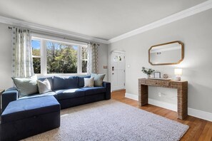 A living room with a blue sofa, a white rug, a wooden floor, a console table with a mirror, and a door leading outside.