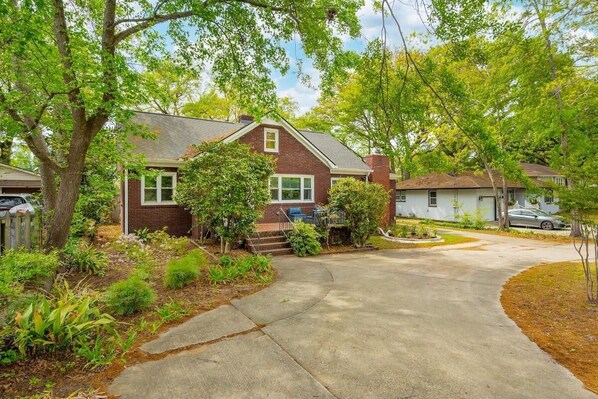 A residential house with a driveway, a front yard with various plants, and a neighboring house.