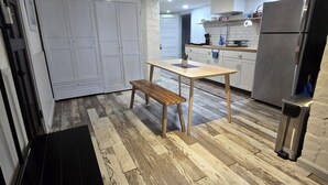 Eine moderne Küche mit Holzboden, einem Esstisch mit einer Bank, einem Kühlschrank und weißen Schränken.