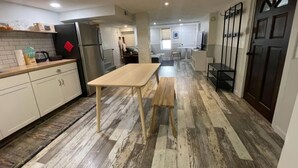 Eine moderne Küche mit weißen Schränken, einem Holztisch und einer Bank. Man sieht einen Kühlschrank, eine Spüle und ein Fenster.