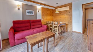 A room with a red sofa, wooden dining table, and chairs. There is a wooden wall with a picture frame and wall-mounted lights. - 40m from ski slopes, fitness, swimming pool, sauna, tv, ski locker, 41m², Les Orres (Les Orres)