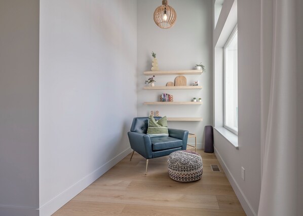 A modern living room with a blue armchair, a round ottoman, and wooden shelves with decorative items.