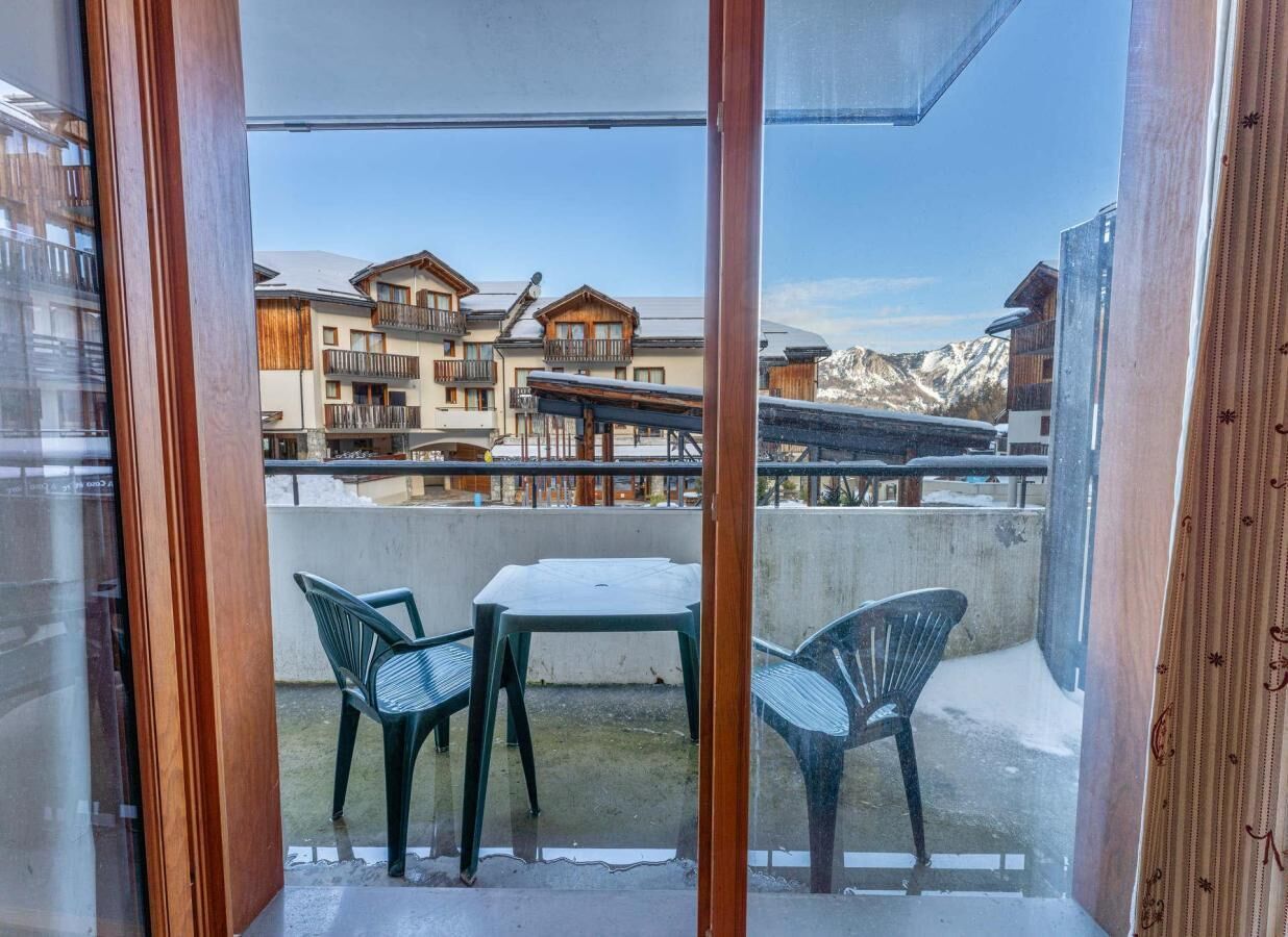 A balcony with a table and chairs, overlooking a mountainous area with buildings.
