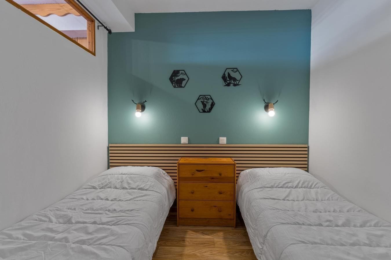 Une chambre avec deux lits, une commode en bois et des lampes fixées au mur.