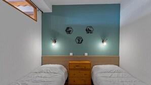 Une chambre avec deux lits, une commode en bois et des lampes fixées au mur.