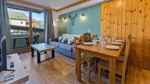 Un salon confortable avec un canapé, une table à manger en bois pour quatre personnes et un balcon offrant une vue sur les montagnes.