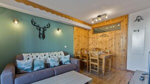 Une pièce chaleureuse avec un canapé, une table à manger et des chaises. Un mur en bois est décoré d’un motif représentant une montagne et d’une tête de cerf.