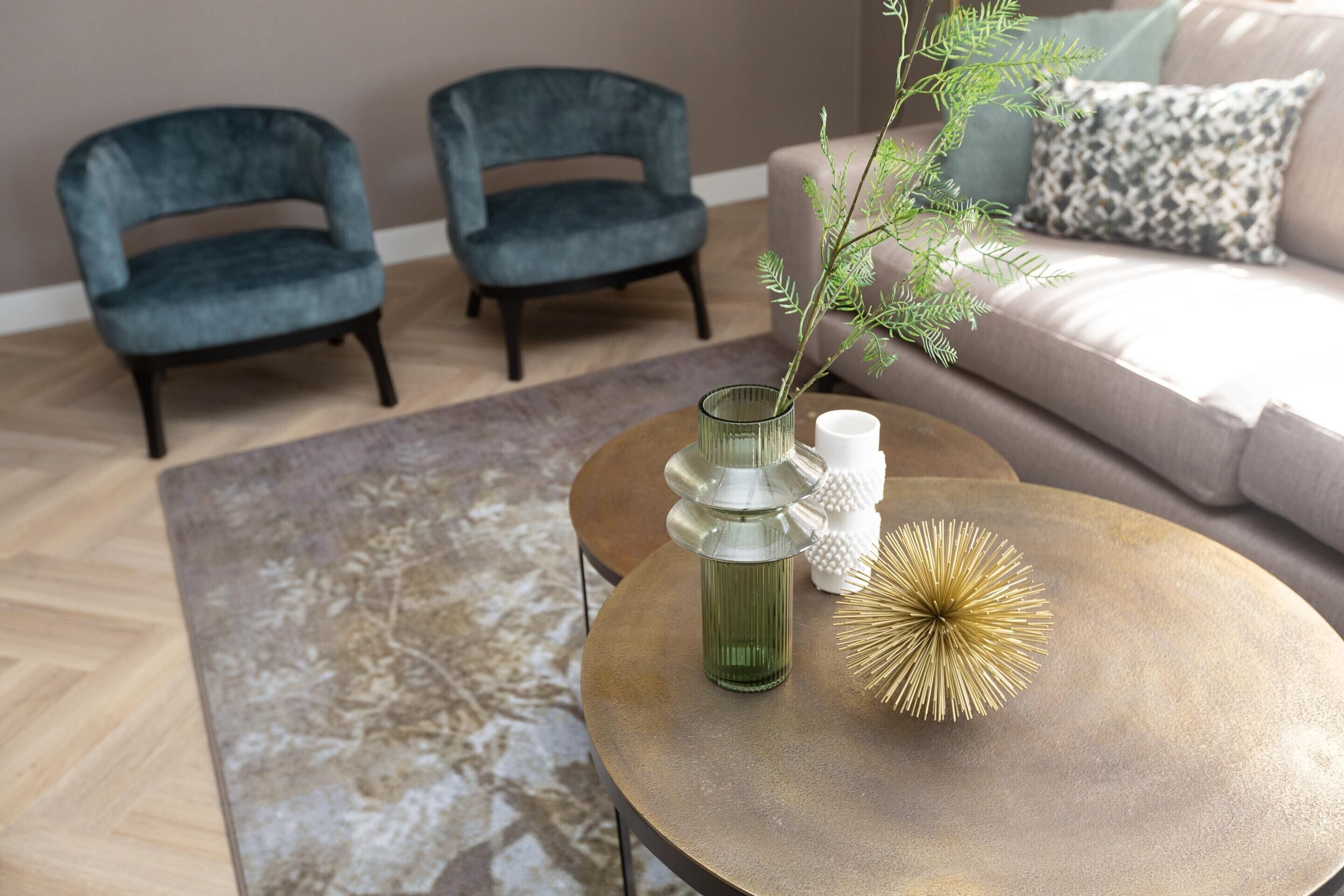 A living room with a round coffee table, two armchairs, a sofa, and a decorative plant.